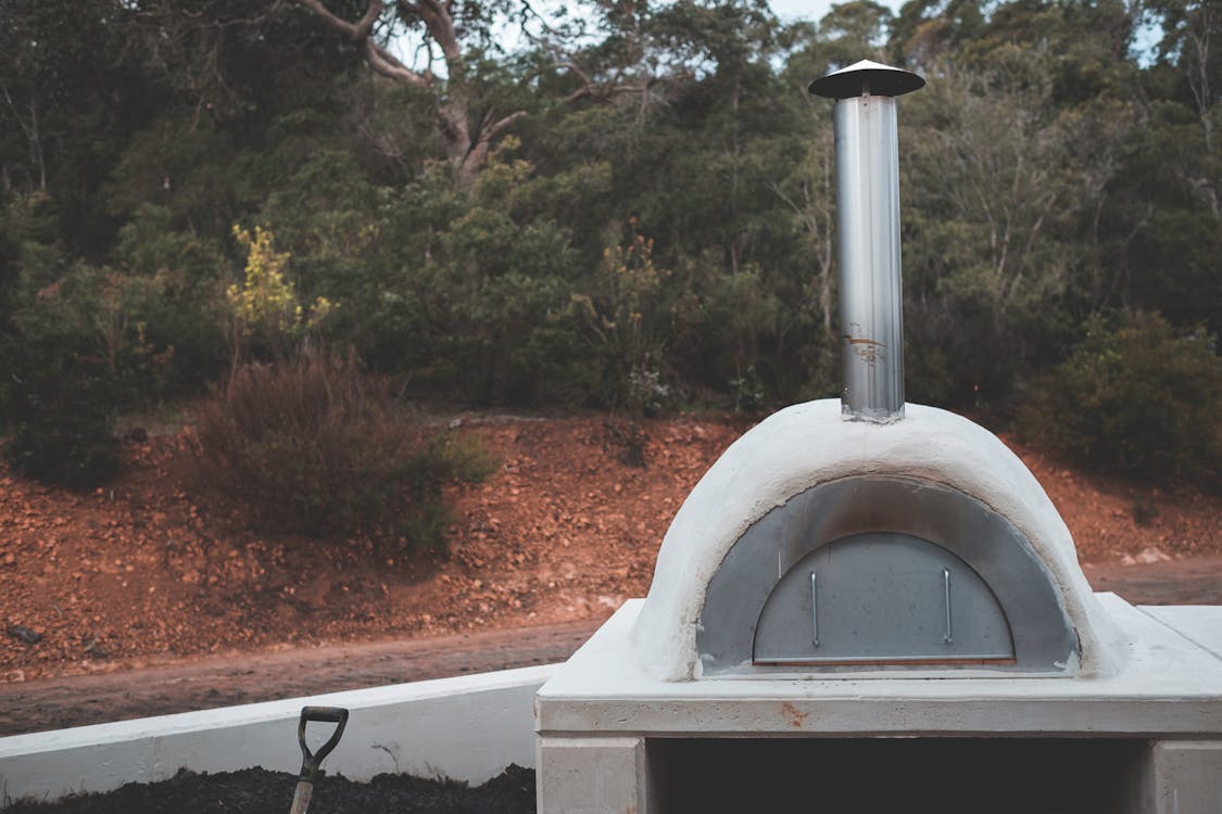 Free Stone pizza oven with stainless flue placed in lush summer garden for picnic Stock Photo