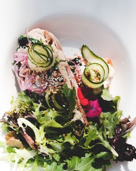 Top view appetizing vegetarian salad with healthy mix leaves and red onions garnished with cucumber served on white plate on sunny terrace