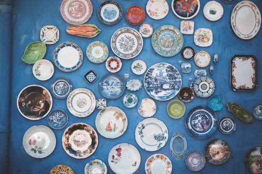 Composition of various decorative ornamental plates of different sizes and colors arranged on blue wall