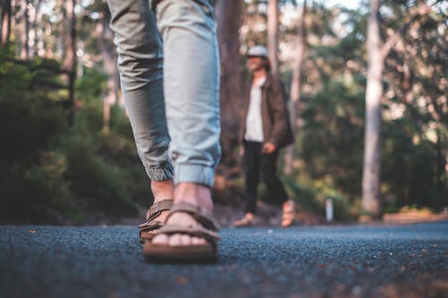 Crop unrecognizable person in sandals walking on asphalt sidewalk
