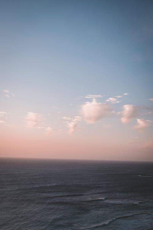 Scenic view of endless tranquil sea rippling beneath clear blue and pink sky in early evening