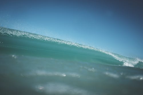 Powerful wave of turquoise ocean with transparent splatters rolling on crystal water in sunny day