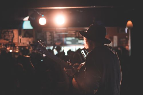 Free Back view of anonymous male artist playing acoustic guitar and singing song on stage during concert in dark club Stock Photo