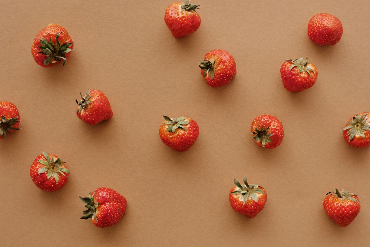 a flat lay of fresh strawberries spread on a brown background perfect