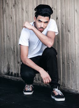 Casually dressed young man squatting in an urban area, blending modern style and attitude.