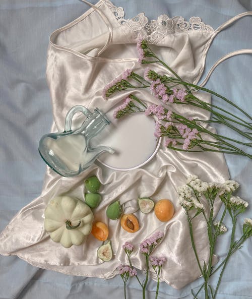 Free From above composition of silk cloth with with fruits and pumpkin placed near glass jug with wildflowers on gray textile Stock Photo