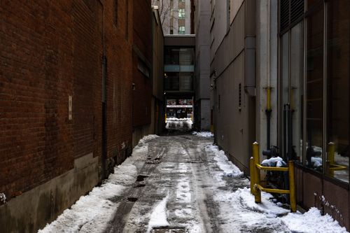 Free A narrow, snow-covered alleyway flanked by brick walls in an urban setting during winter. Stock Photo