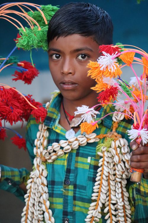 Free South Asian boy in colorful attire holding vibrant handmade decorations outdoors. Stock Photo