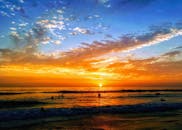 在平静的海面上，游泳者剪影映衬着充满活力的日落，景色令人叹为观止