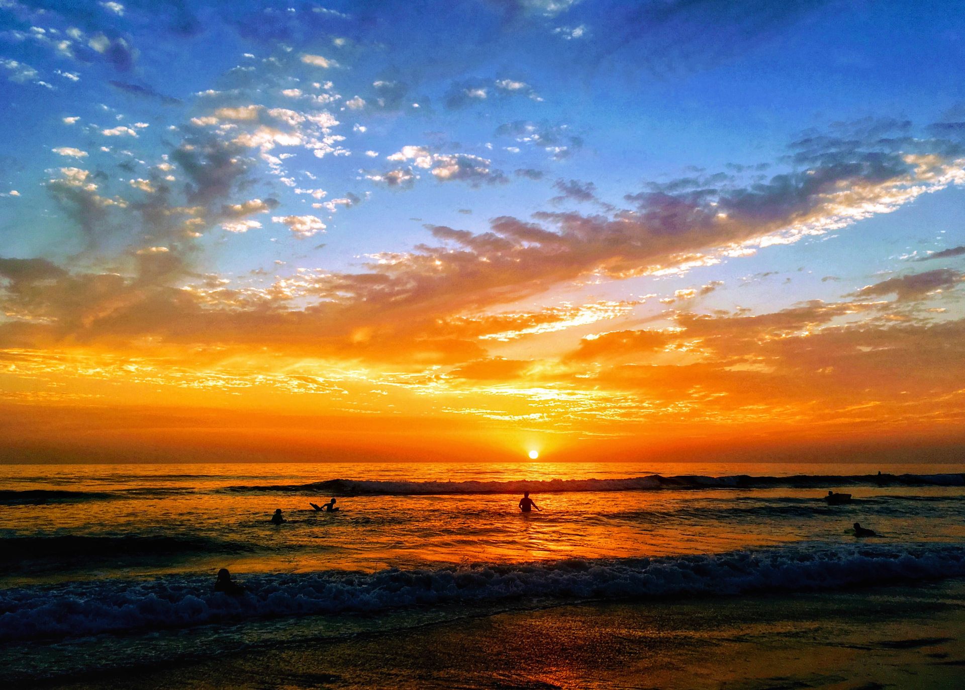 Breathtaking view of a vibrant sunset over a peaceful ocean with silhouettes of people swimming.