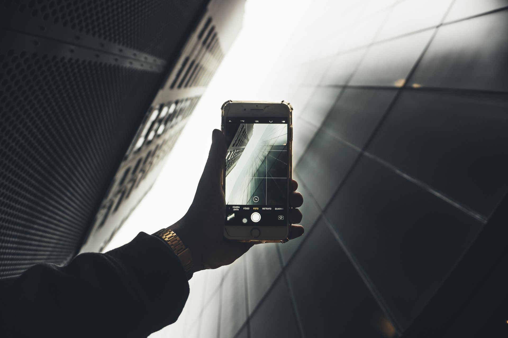 A hand holding a smartphone capturing reflections of sleek modern architecture.