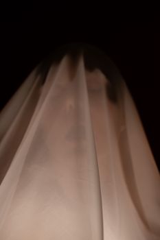 万圣节庆祝活动期间，暗室的黑色背景前，一位张着嘴的幽灵女性肖像站在白色透明布下