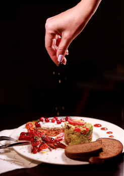 A hand seasons a gourmet meal with precision, adding final touches to a plated dish.