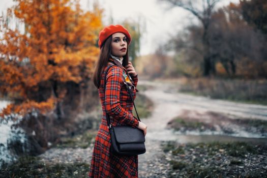 Woman in a plaid dress and red beret walking on an autumn path in Ankara, Türkiye.