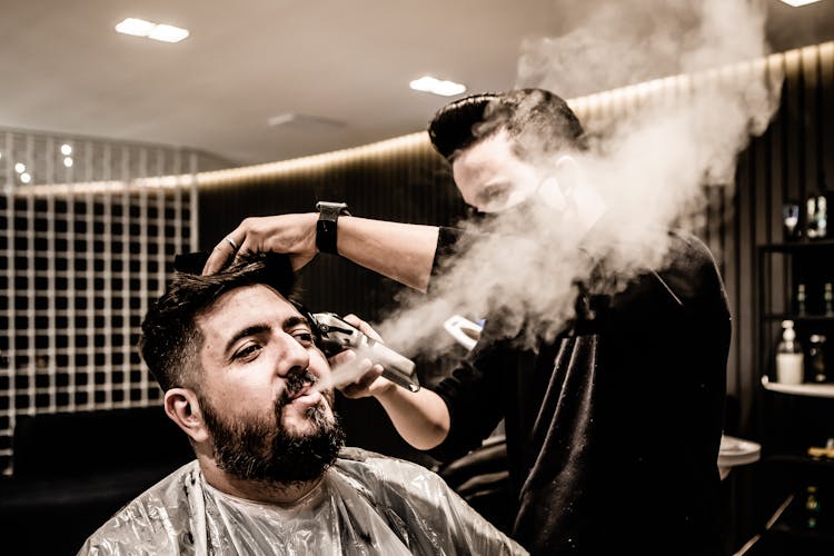 
A Bearded Man Blowing Smoke While Having A Haircut