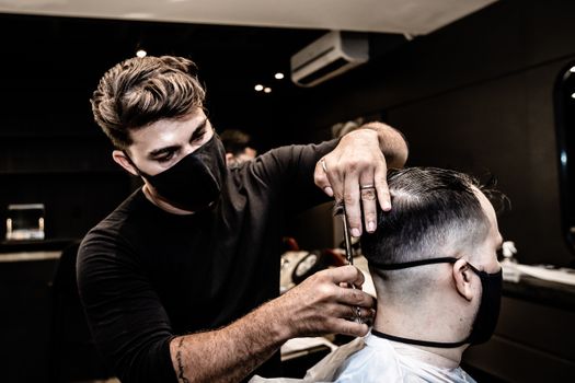 Professional barber wearing a mask giving a haircut in a modern barbershop setting.