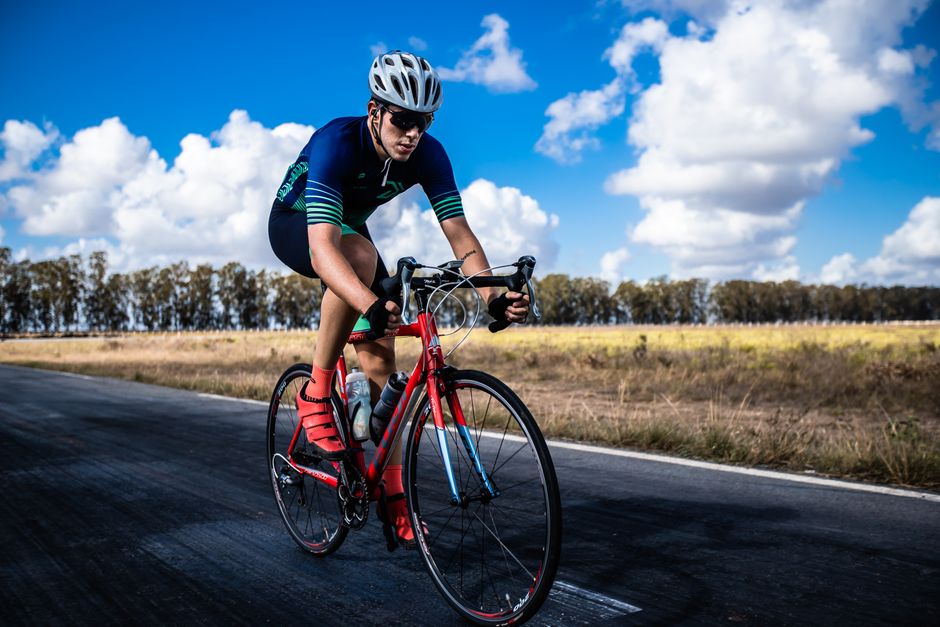 A focused cyclist in a helmet riding on a country road under a vibrant sky.