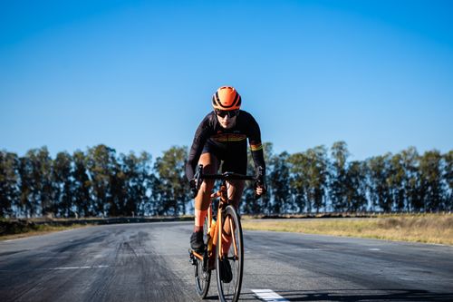 Free A cyclist on an orange bike riding on an open road under a clear blue sky in João Pessoa, Brazil. Stock Photo