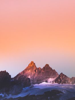 Sunrise over Swiss mountains with orange sky, showcasing snow-covered peaks and a serene atmosphere.