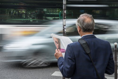 Free Man Wearing Blue Suit Jacket Holding Newspaper in Front Vehicle on Concrete Road Stock Photo