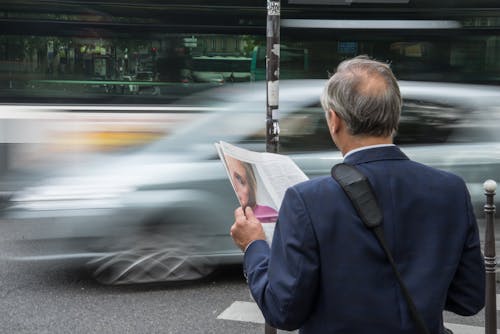 Man Wearing Blue Suit Jacket Holding Newspaper in Front Vehicle on Concrete Road