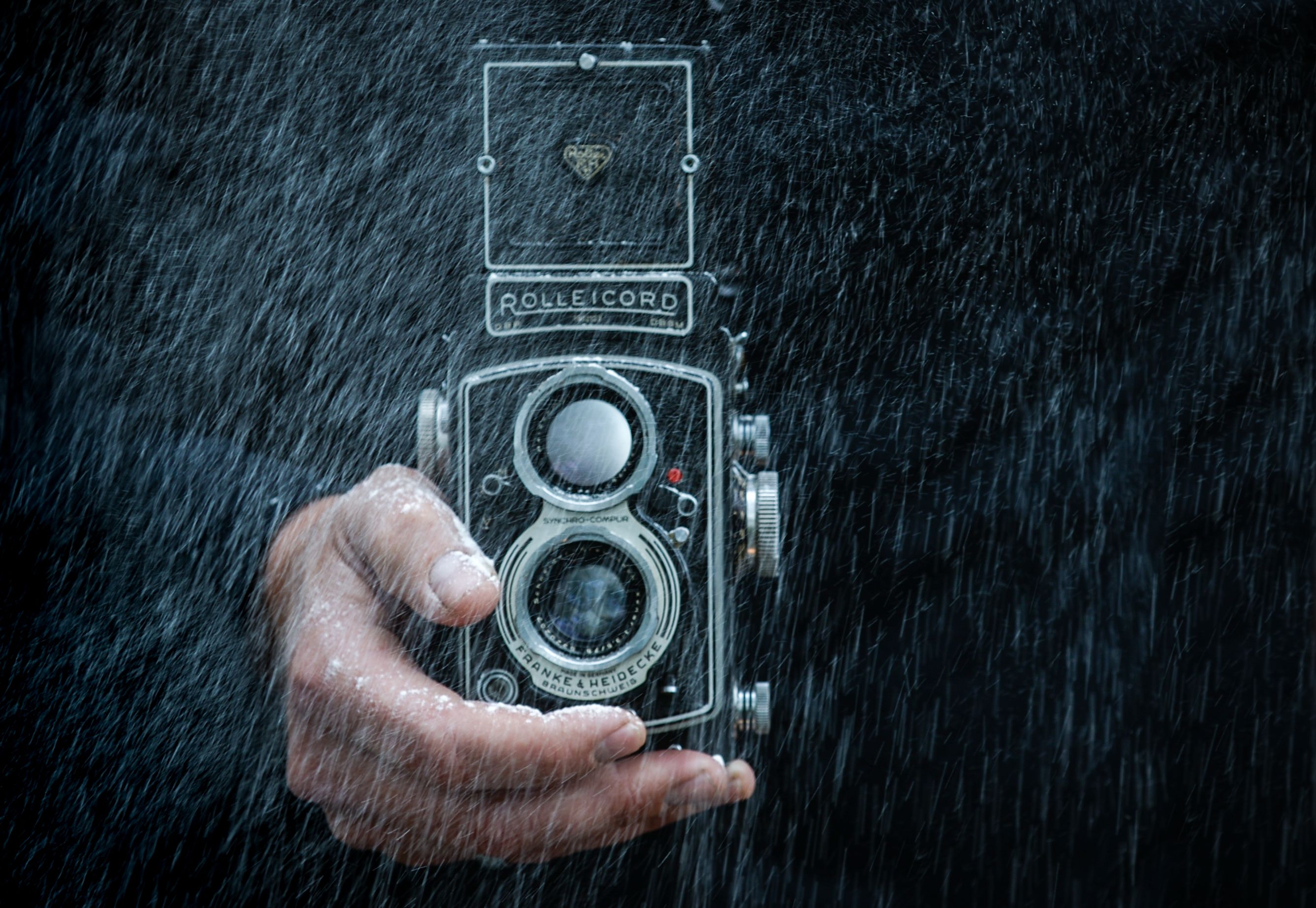 Close-up of a vintage Rolleicord camera held in hand under rain.