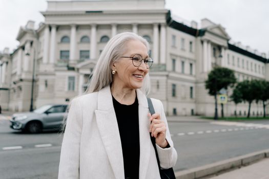 一位身穿白色夹克衫的老妇人，在一座历史建筑附近微笑着散步