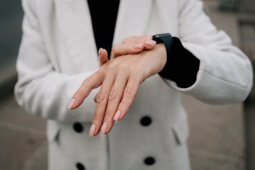 Close-up of a woman checking her smartwatch outdoors, wearing a white coat and manicured nails.