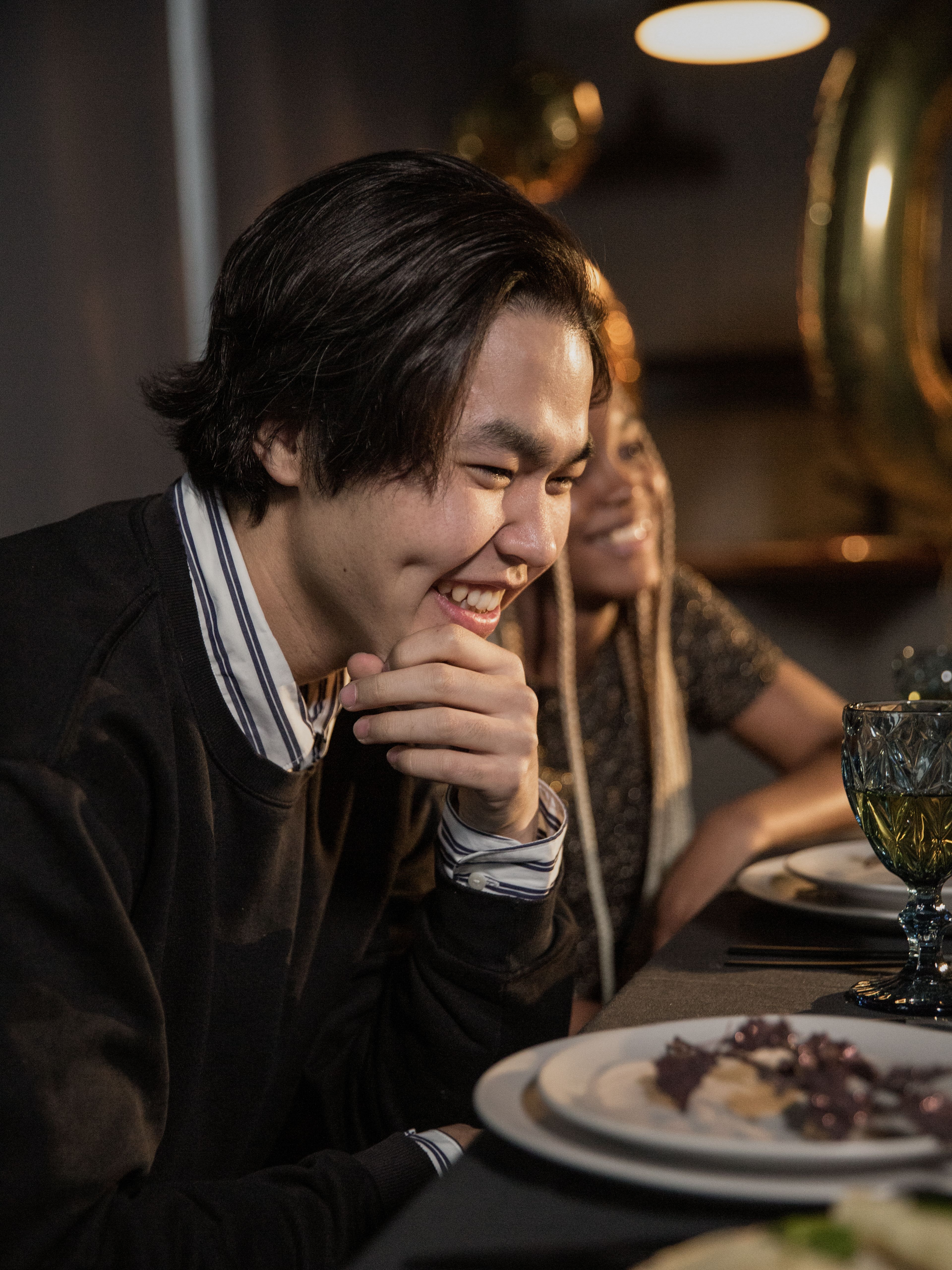 Fotomural Dos jóvenes sentados en una mesa, sonriendo y disfrutando de una comida en el interior.
