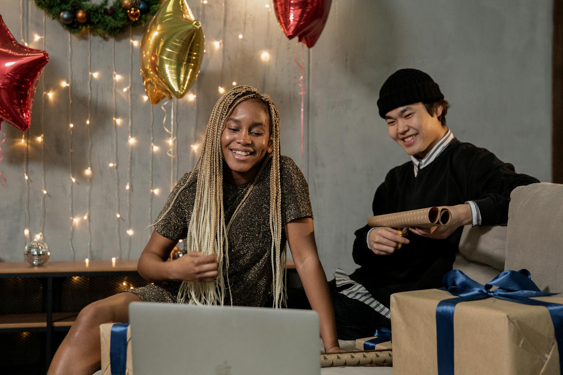 Two friends enjoying an online holiday party with gifts and festive decor.