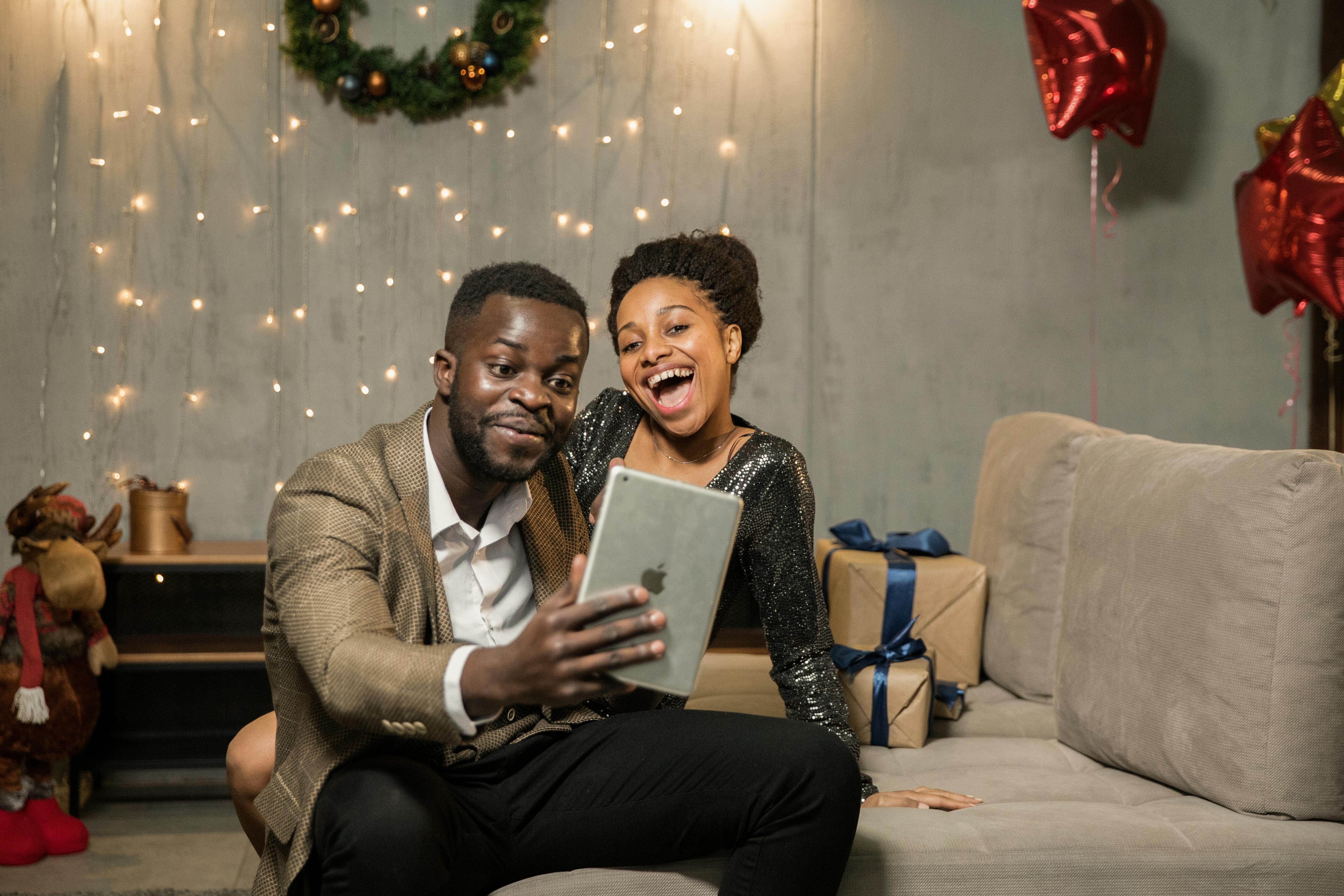 A joyful couple at home, video calling during a festive holiday celebration with gifts and decorations.