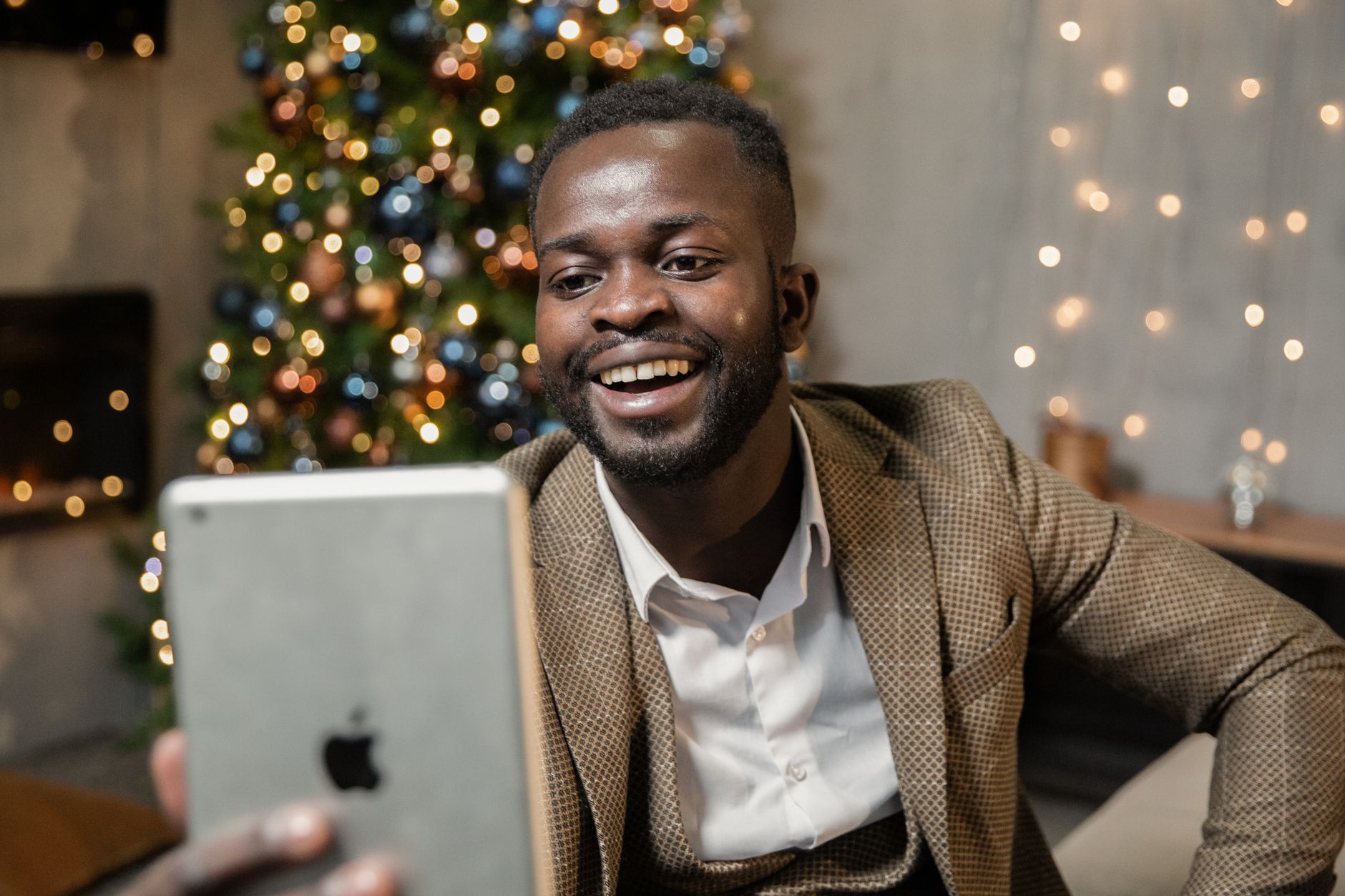 Cheerful man using a tablet for video call at a Christmas party, smiling in a festive setting.