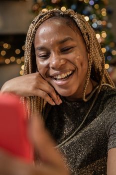 A happy woman having a video call on her smartphone with Christmas decorations in the background.