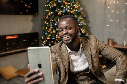 Free Cheerful man enjoys a video call near a Christmas tree, spreading holiday joy and connection. Stock Photo