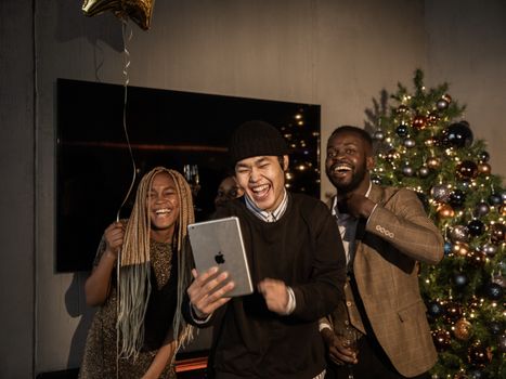 A diverse group enjoys a cheerful video call at a festive Christmas party, with decorations and a tree.
