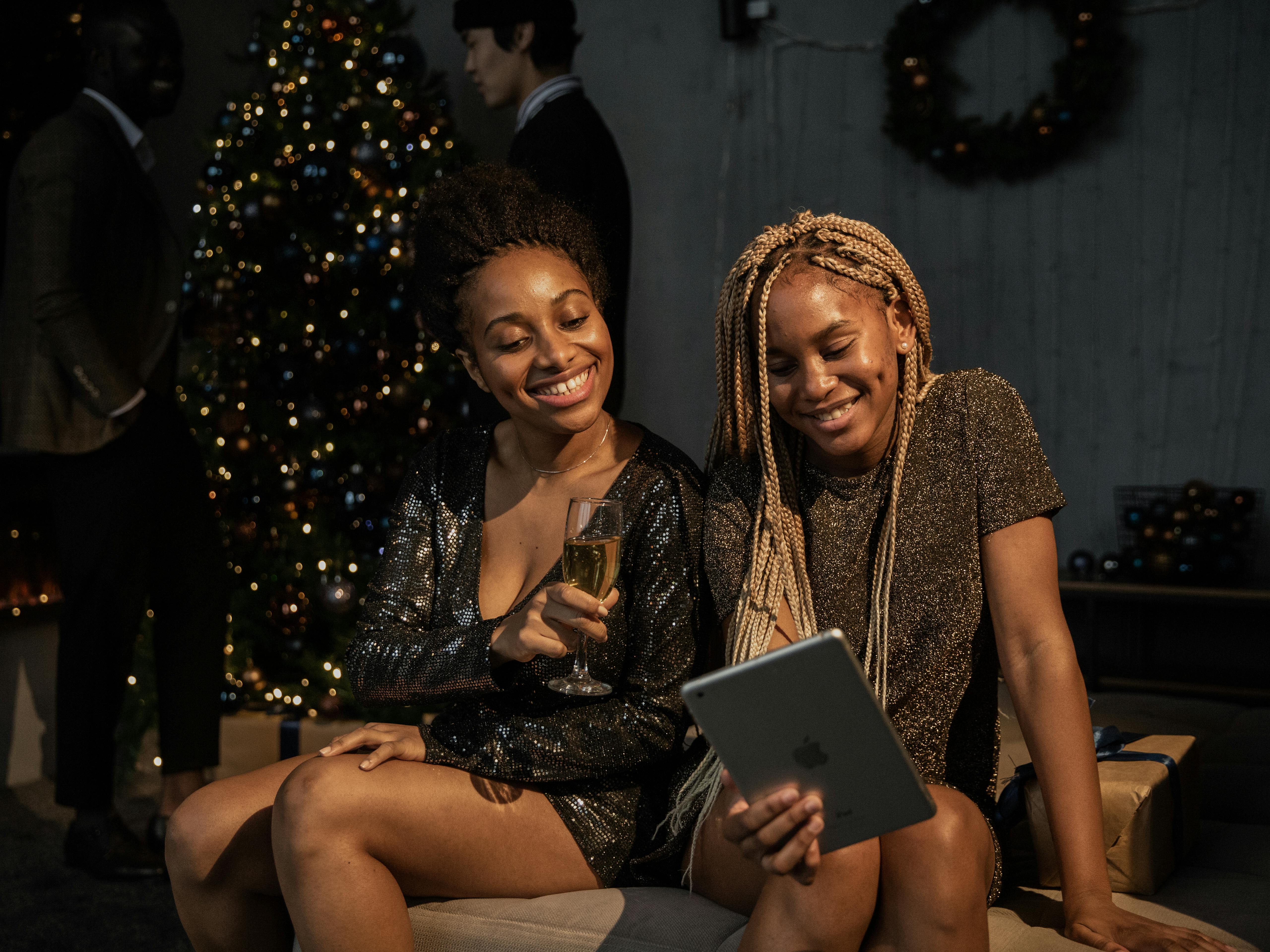 Two young women enjoy a Christmas party, smiling and video chatting amid festive decor.