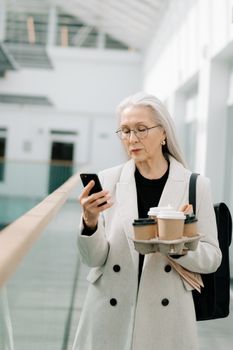 一位老年妇女在室内一边喝咖啡一边用智能手机发短信，享受着现代技术带来的便利