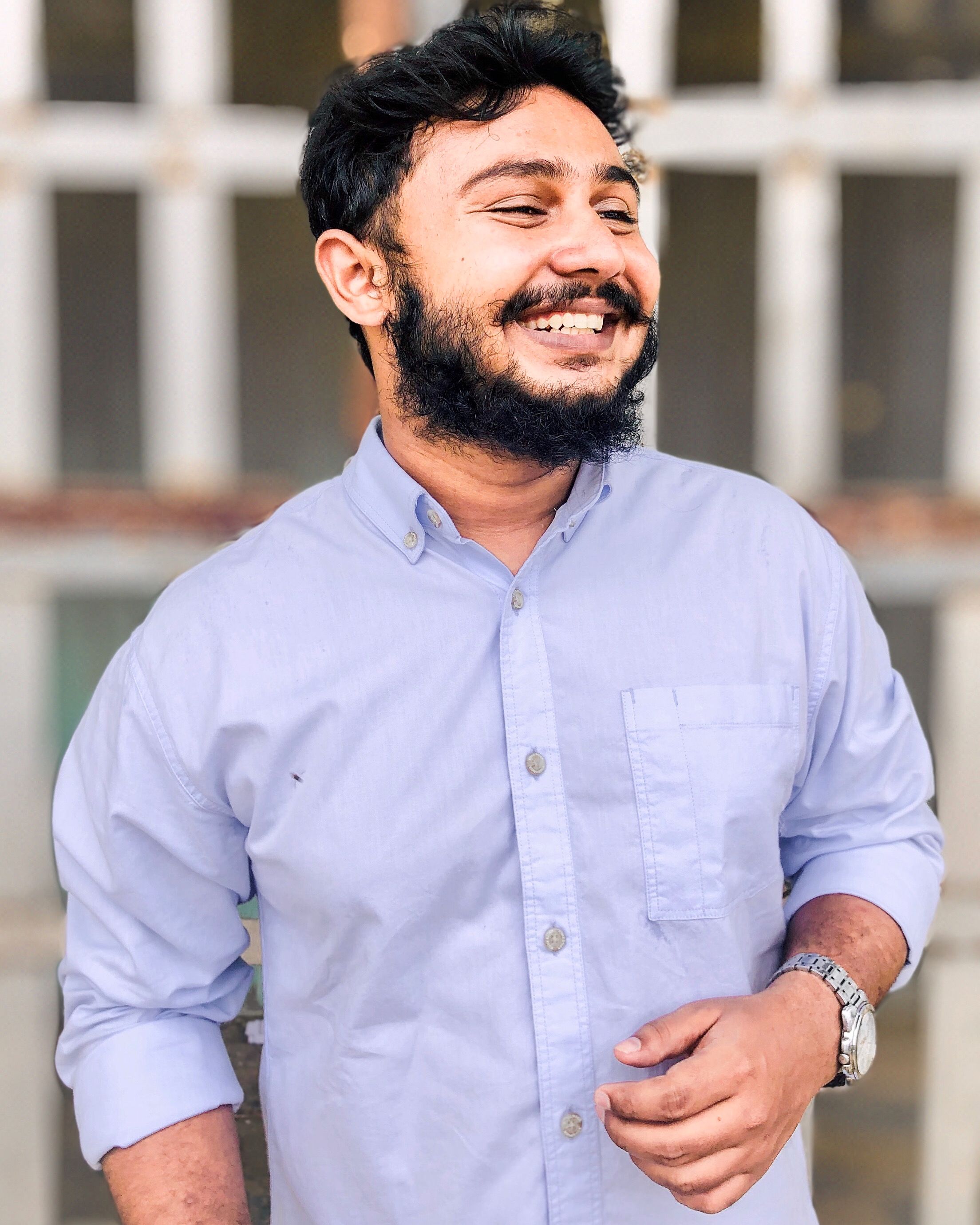 Portrait of a happy bearded man wearing a casual shirt and watch, smiling outdoors.