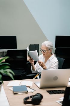 一位老年女商人在现代办公桌前审查文书工作