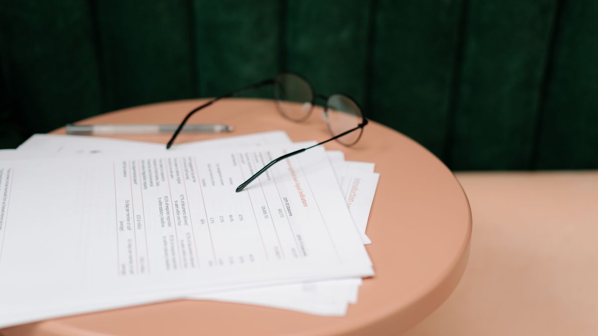 A close-up of documents, eyeglasses, and a pen on a round table indoors.