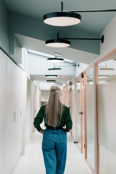 一个女人从现代办公室走廊走过的后视图，展现了当代设计