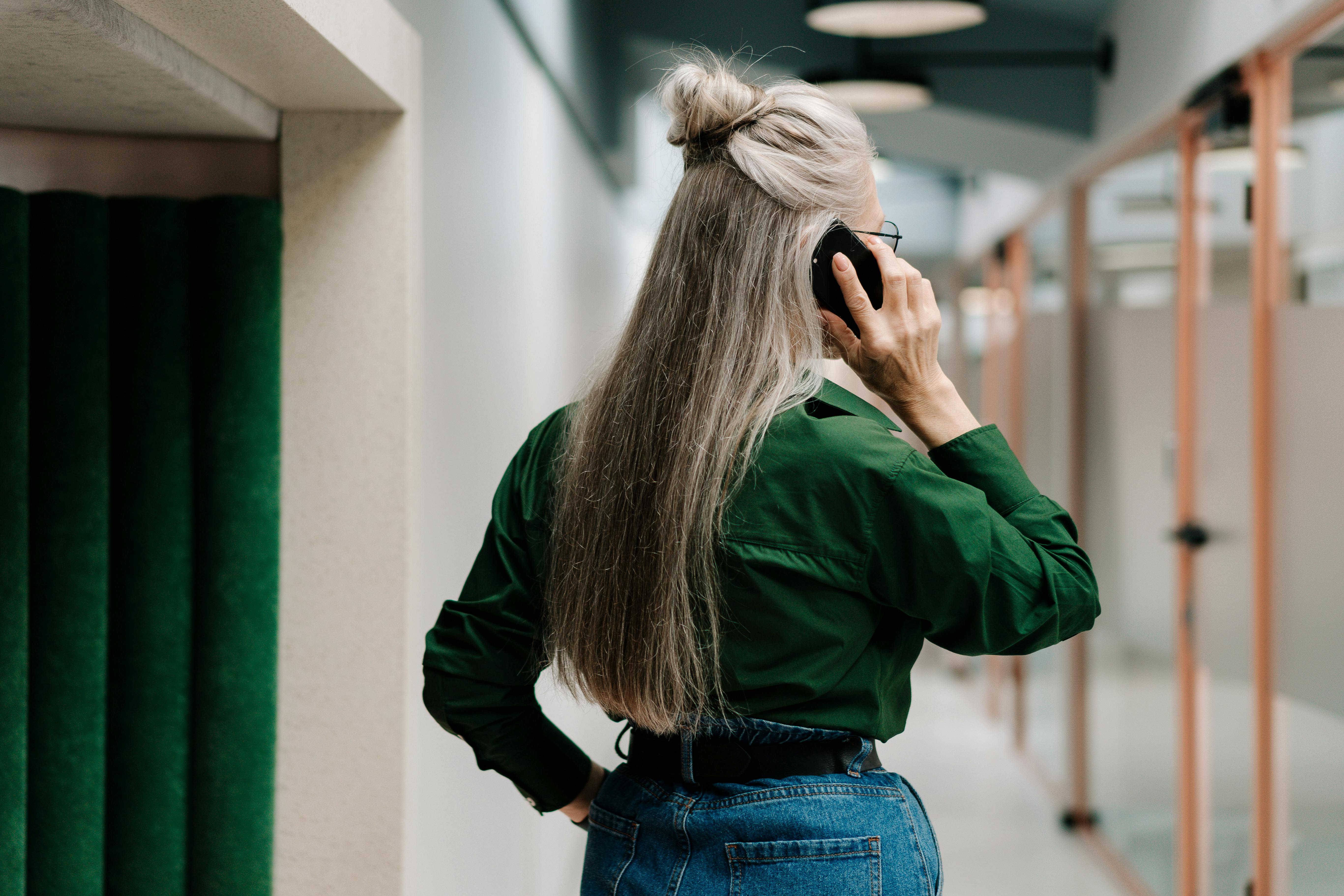 Rear view of a senior woman talking on a smartphone in a contemporary office setting.