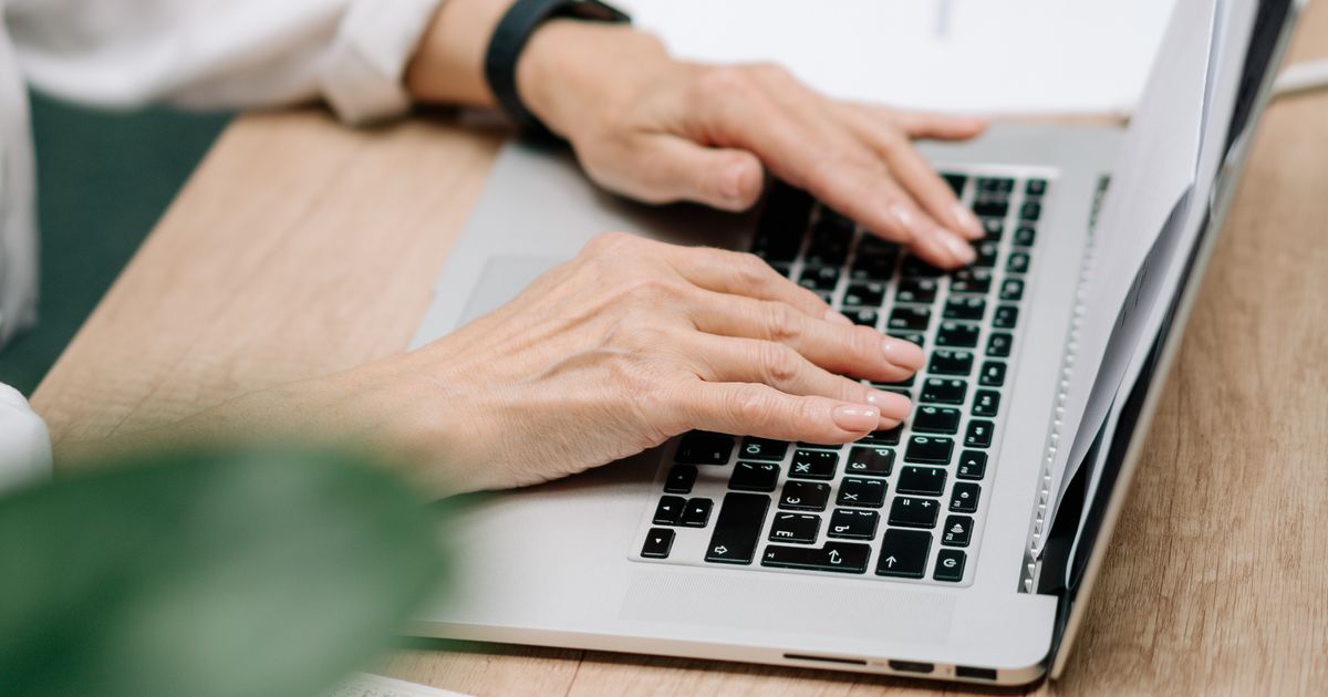 Close-up of a professional's hands typing an email reply on a laptop at a wooden desk