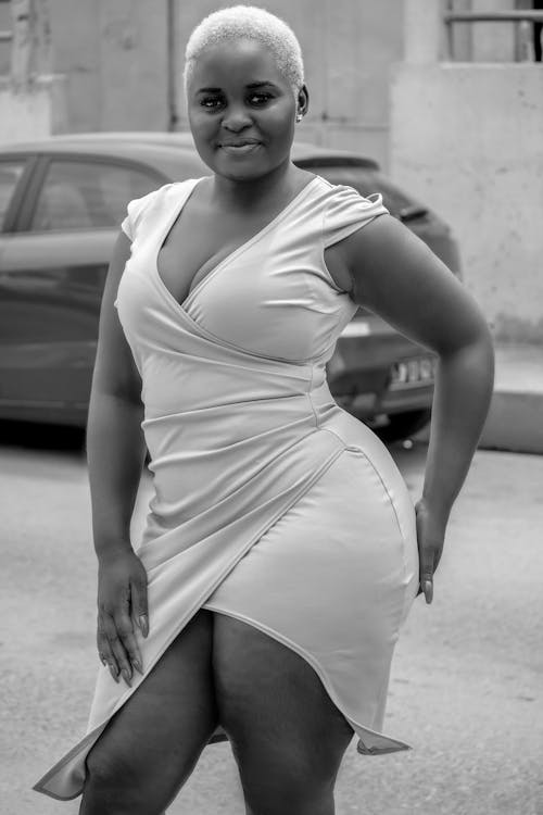 Black and white of plus size African American female with short hairstyle in dress looking at camera on street