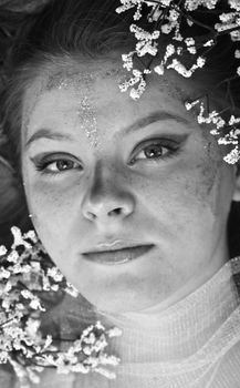 Artistic black and white portrait of a young woman adorned with delicate flowers and glitter.