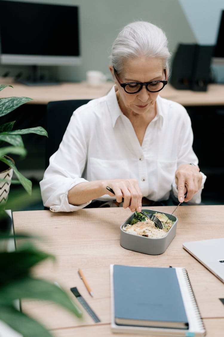 Elderly Woman Eating Packed Lunch At The Office