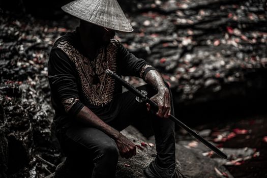 A dramatic outdoor portrait of a man holding a samurai sword, wearing traditional attire with a hat.