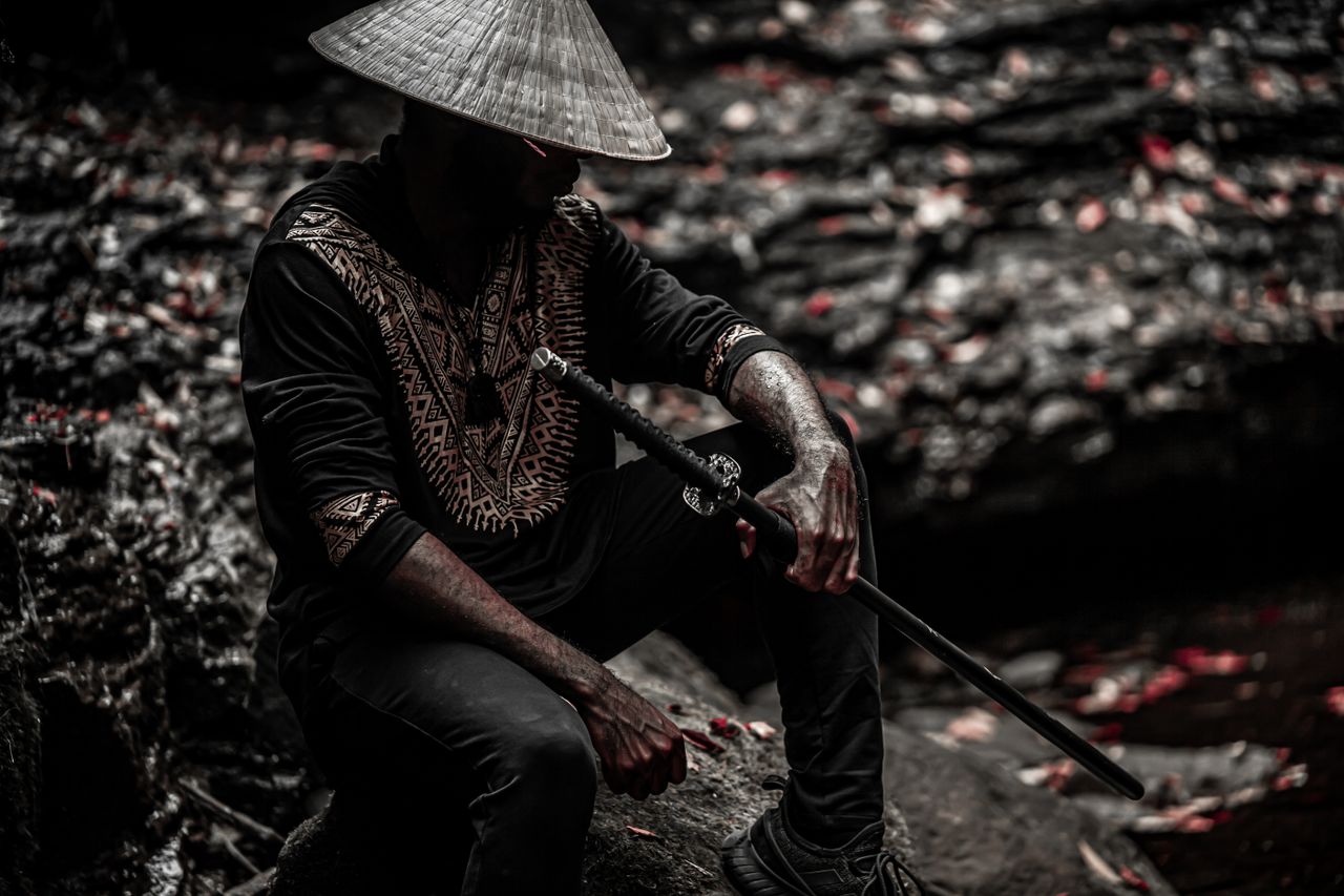 a dramatic outdoor portrait of a man holding a samurai sword wearing t