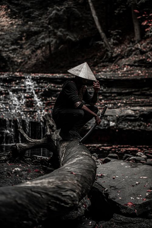 Free A mysterious samurai sits by a quiet waterfall, sword in hand. Stock Photo
