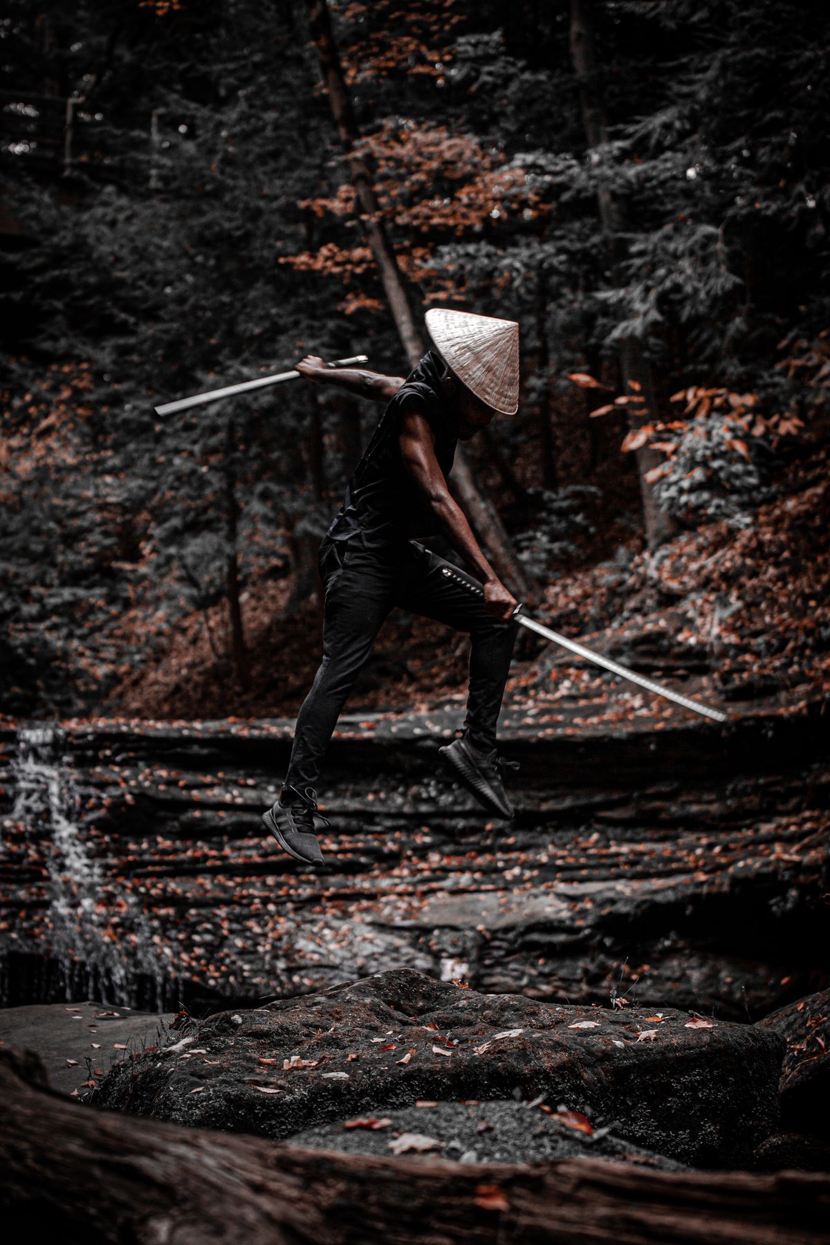 Person in a conical hat jumping with a sword in a forest
